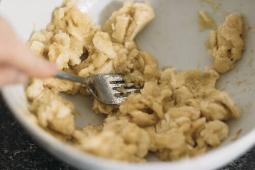 Zerdrückte Bananen mit Gabel in Schüssel.