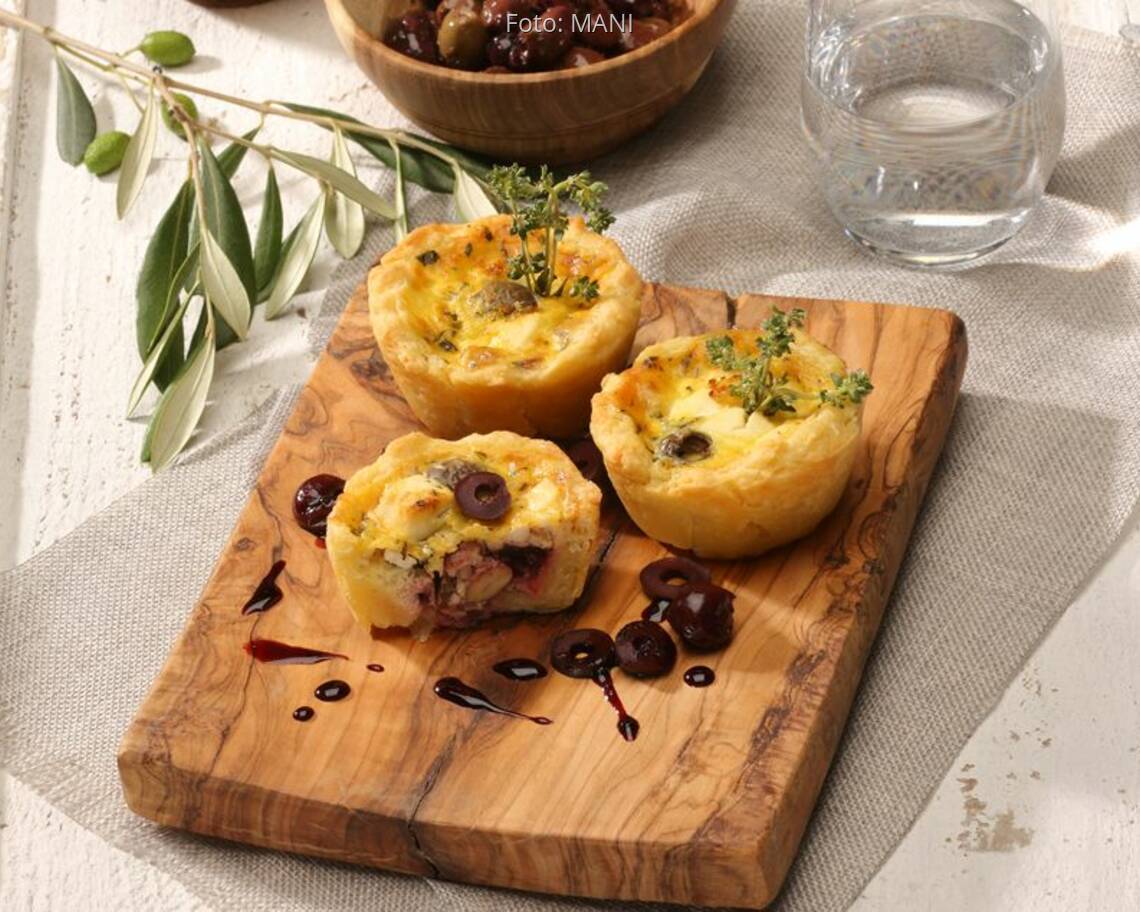 Käsemuffins auf Holzbrett mit Kirchen und Oliven