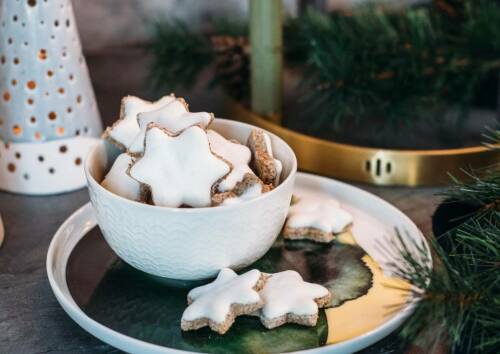 Klassische Zimtsterne mit weißer Haube schön auf einem Teller angerichtet, daneben Tannenzweige. Von vorne fotografiert.