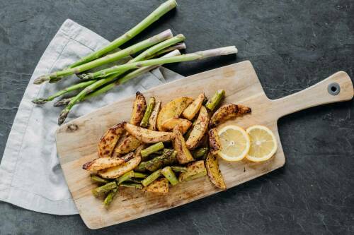 Zitronenkartoffel mit Spargel auf Schneidebrett und Geschirrtuch vor dunklem Hintergrund.