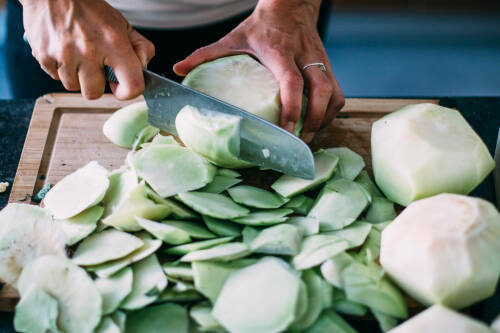 Kohlrabi schälen mit einem scharfem Messer auf einem Schneidebrett.