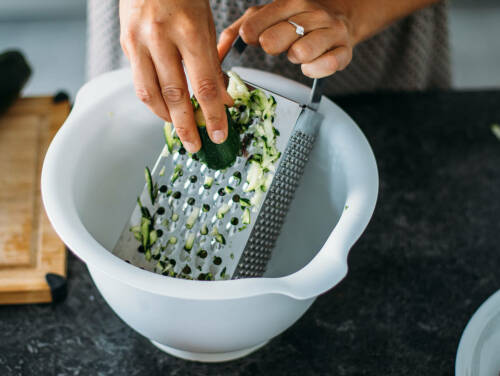 Zucchini wird in eine Schüssel geraspelt.