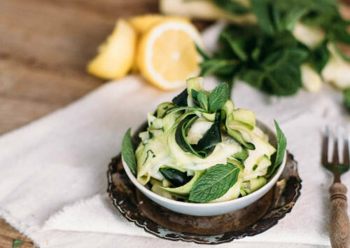 Zucchini-Minz-Salat in einer Schüssel im Hintergrund Zitrone und Besteck, von der Seite fotografiert