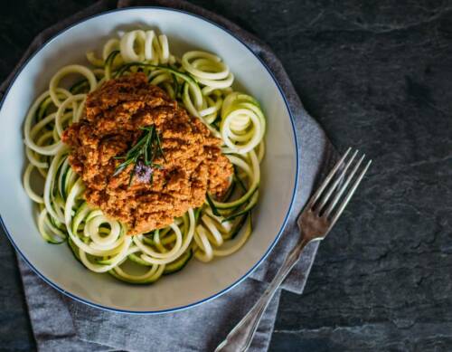 Zucchini Nudeln mit Walnusspesto in Teller vor dunklem Hintergrund.