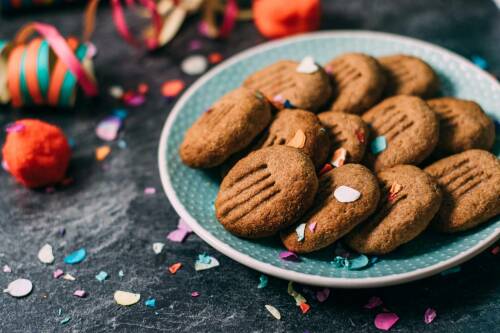 Zuckerarme Bärentatzen auf blauem Teller neben buntem Konfetti vor dunklem Hintergrund.
