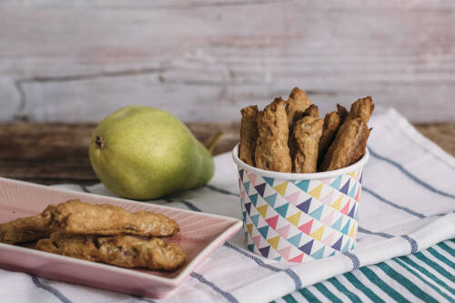 Zuckerfreie Birnen Dinkel Stangen in Partybecher neben Birne vor hellem Hintergrund.
