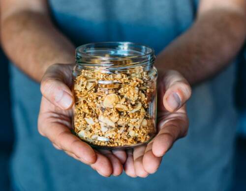Zuckerfreies Müsli in Weckglas und zwei Händen vor dunklem Hintergrund.
